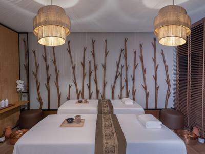 Modernes Spa-Zimmer mit zwei Massageliegen und natürlicher Holzdeko an der Wand.