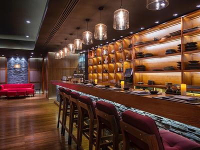 Moderne Bar mit dunklem Holz, roten Stühlen, beleuchteten Regalen und warmem Ambiente.