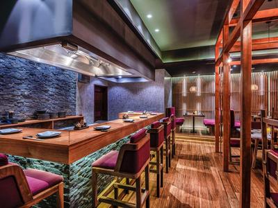 Modernes Restaurant mit Holzmöbeln, dunklen Wänden und beleuchteter Bar in warmem Ambiente.