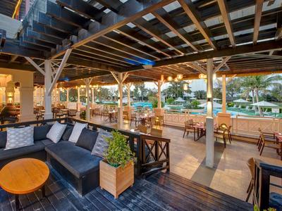 Außenbereich einer Hotelbar mit Lounge-Möbeln und Blick auf den Pool bei Sonnenuntergang.