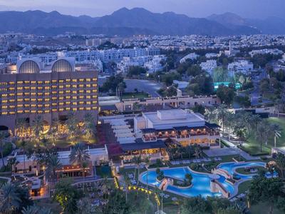 Luxushotel mit Pool und Gartenlandschaft vor Bergkulisse bei Dämmerung.