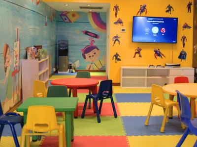 Bunter Kinderspielraum mit farbigen Tischen, Stühlen, gepolstertem Boden und Wanddekoration.