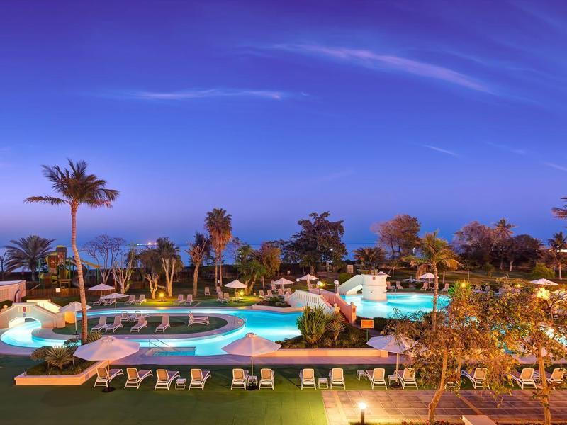 Vue du soir d'une piscine d'hôtel éclairée avec des palmiers et des chaises longues