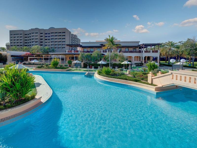 Grand bassin d'hôtel avec eau claire et bleue entouré de végétation par temps ensoleillé.