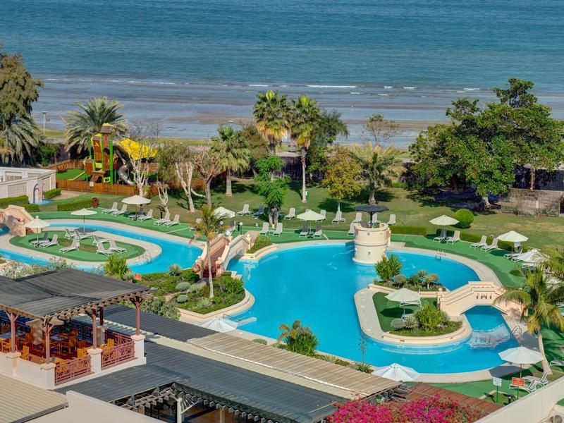 Aire de piscine d'hôtel avec toboggans, parasols et vue sur la plage et la mer.