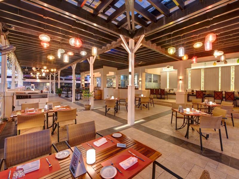 Espace restaurant extérieur ouvert, éclairé avec style, avec des tables en bois et une ambiance conviviale.