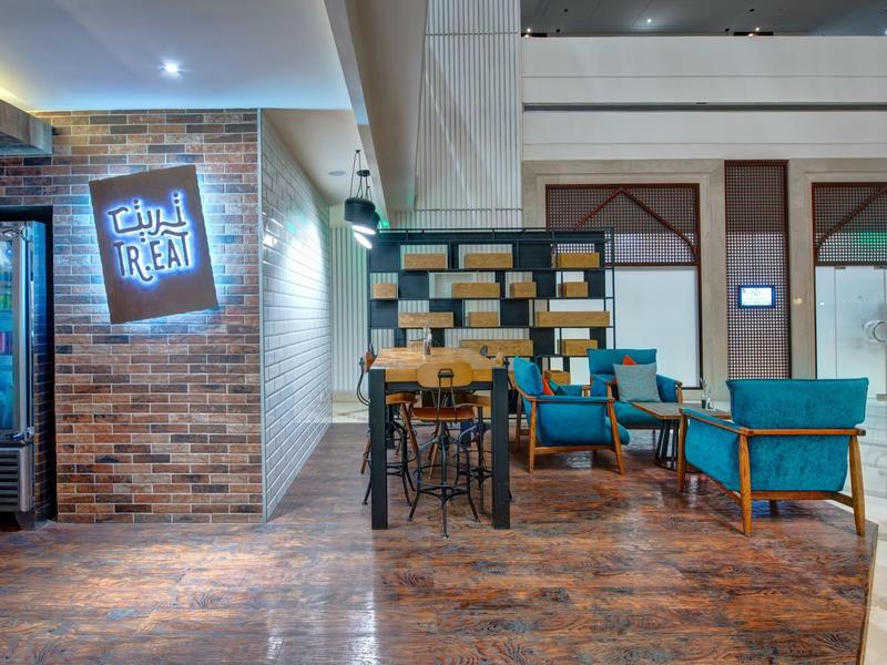 Restaurant d'hôtel moderne avec tables en bois, chaises bleues et décoration murale éclairée.