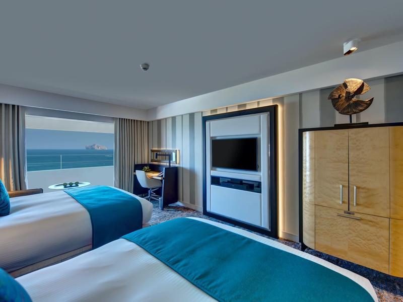 Chambre d'hôtel moderne avec deux lits, vue sur la mer et décoration élégante en bois et bleu.