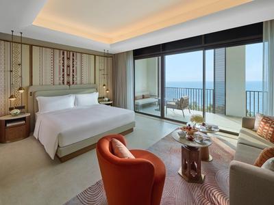 Piscine moderne d'hôtel entourée de chaises longues, parasols et palmiers par une journée ensoleillée.