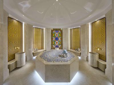 Salle de spa ronde et luxueuse avec carreaux de mosaïque, murs élégants et éclairage indirect.