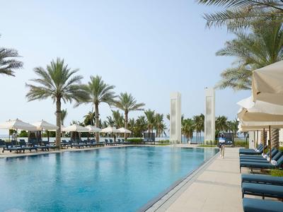 Moderner Außenpool mit Liegestühlen und Sonnenschirmen in einer Hotelanlage unter Palmen.