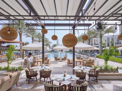 Espace piscine d'hôtel ouvert avec tables, chaises et vue sur la mer en plein jour.