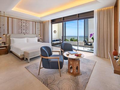 Chambre d'hôtel moderne avec lit double, coin salon et balcon avec vue sur la mer.