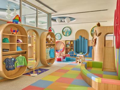Salle de jeux colorée pour enfants avec étagères en bois, tapis multicolore et coin salon lumineux.