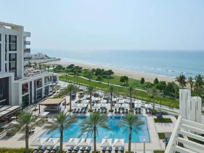 Hôtel avec piscine, parasols et chaises longues à côté d'une plage surplombant la mer.