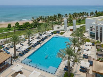 Grande piscine avec chaises longues près de la plage et vue sur la mer sous un ciel dégagé.