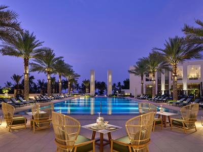 Espace piscine élégant d'un hôtel avec palmiers et sièges confortables au crépuscule.