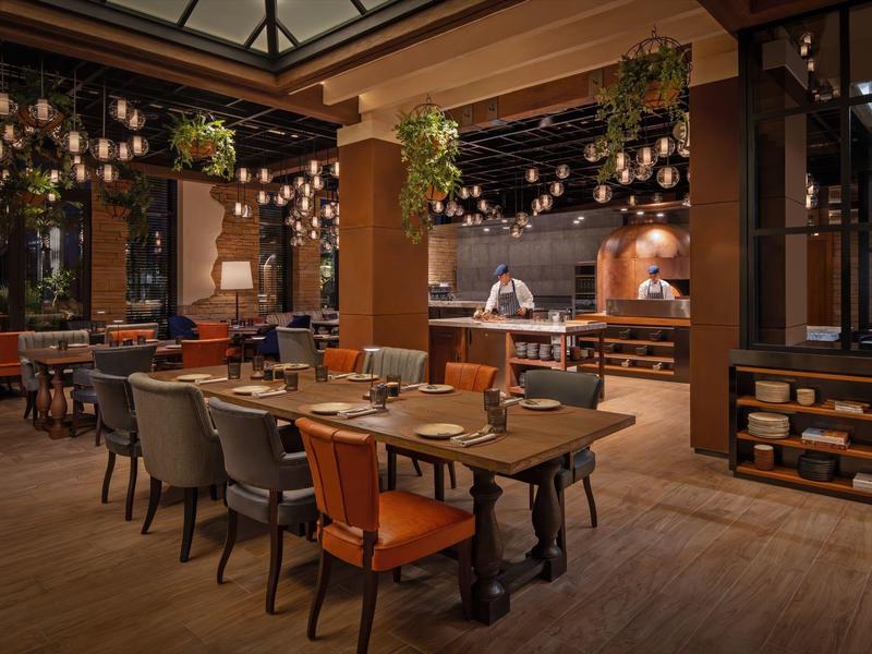 Espace repas confortable avec longues tables en bois, chaises multicolores et éclairage chaleureux.