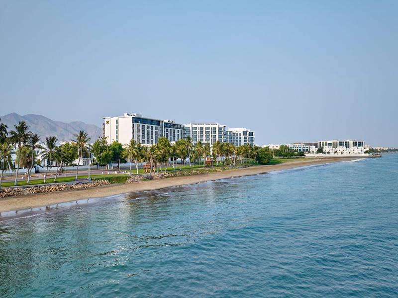 Vue d'un complexe hôtelier au bord de la mer avec des palmiers et un ciel clair en arrière-plan.
