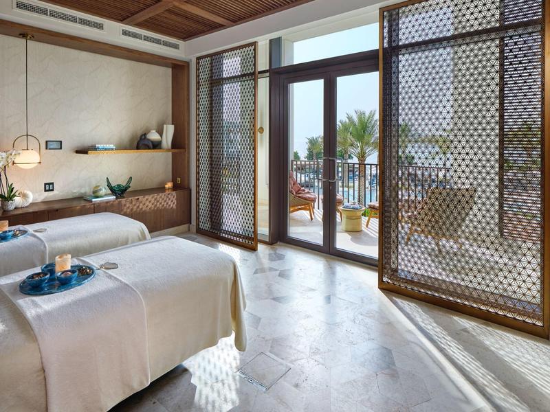 Chambre d'hôtel moderne avec deux lits et grande fenêtre donnant sur une terrasse et des palmiers.