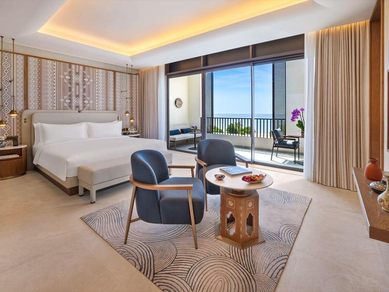 Chambre d'hôtel moderne avec lit double, coin salon et balcon avec vue sur la mer.