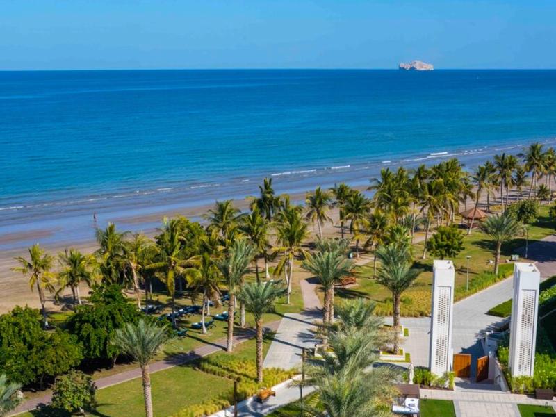 Plage et palmiers avec une piscine d'hôtel au premier plan par une journée ensoleillée.