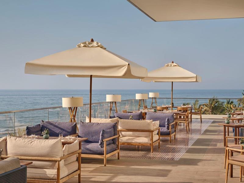 Terrasse avec sièges et parasols surplombant la mer par ciel clair.