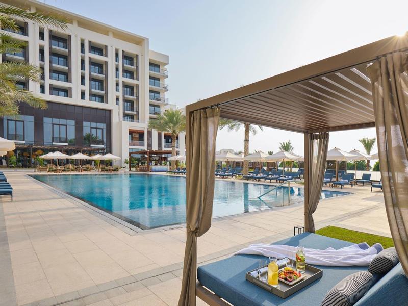 Une piscine d'hôtel moderne avec des transats et une cabane ombragée par temps ensoleillé.