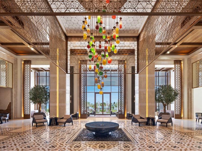 Lobby d'hôtel luxueuse avec grandes fenêtres, éclairage design et espaces de sièges élégants.