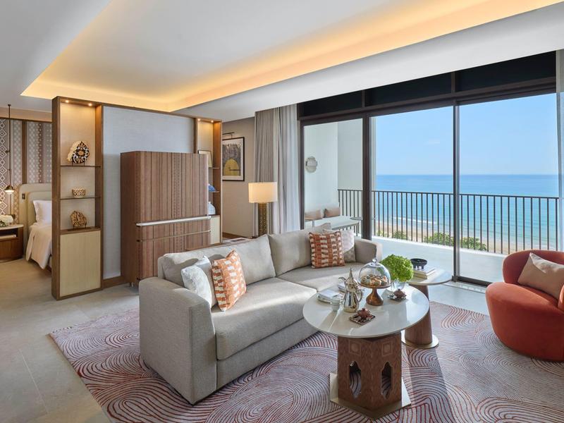 Chambre d'hôtel moderne avec canapé, fauteuils et balcon avec vue sur la mer.