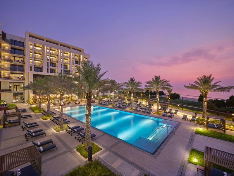 Piscine moderne d'hôtel au coucher du soleil avec palmiers et chaises longues
