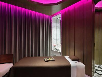 Ošetřovna s masážním lehátkem, závěsy a ambientním fialovým osvětlením.