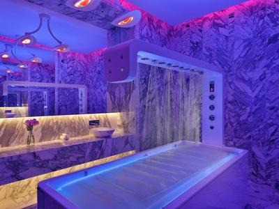 Moderní spa s modro-fialovým osvětlením, vanou a dekorativními stěnami.