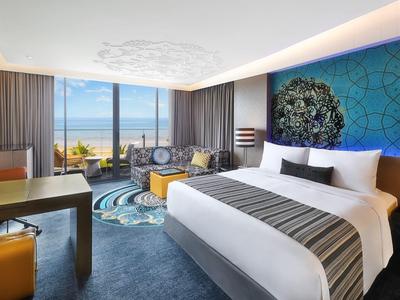 Moderní hotelový pokoj s velkou postelí, psacím stolem a výhledem na moře přes velká okna.