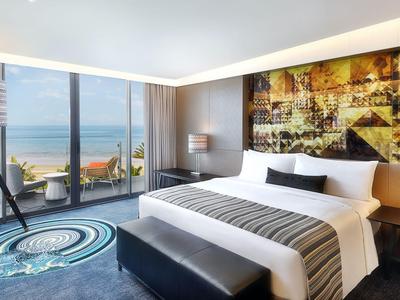 Chambre d'hôtel moderne avec grand lit, fenêtres panoramiques et vue sur la mer.