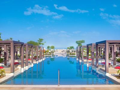 Symmetrischer Außenpool mit blauen Liegen, Palmen und klarem Himmel im Hintergrund.