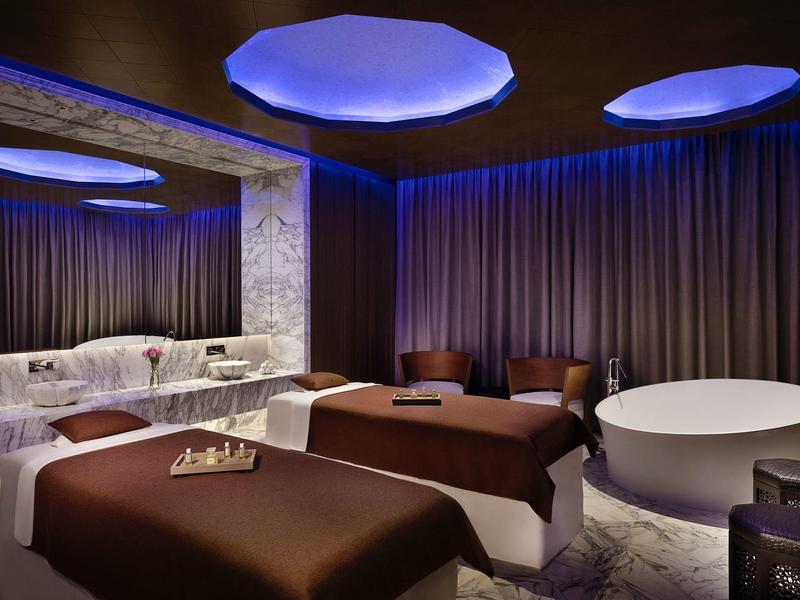 Luxusní spa místnost s masážními lehátky, vanou a tlumeným modrým osvětlením.