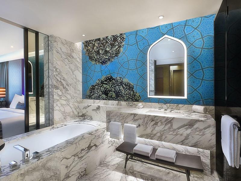 Elegantní koupelna s mramorem, modrým vzorem na stěně a velkým zrcadlem v hotelovém pokoji.