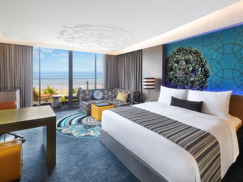 Moderní hotelový pokoj s velkou postelí, psacím stolem a výhledem na moře přes velká okna.