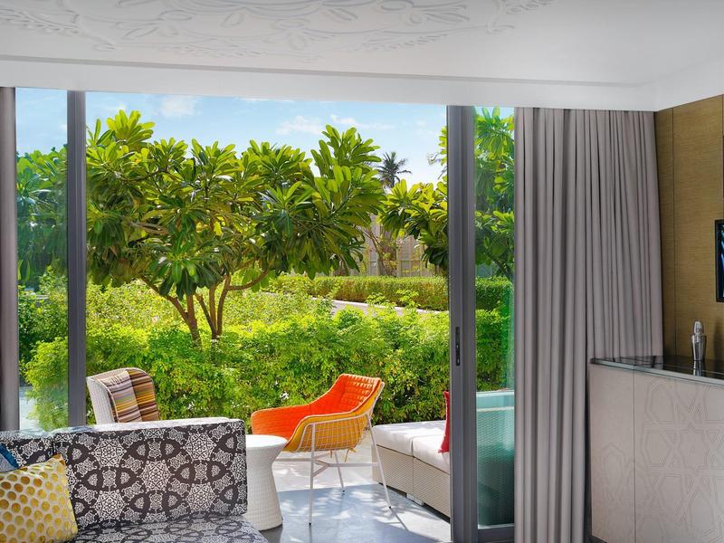 Hotelový pokoj s terasou s výhledem na zelenou zahradu s stromy za slunečného dne.