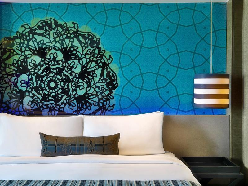 Moderní ložnice s velkou postelí, modrou nástěnnou dekorací a pruhovanou lampou.