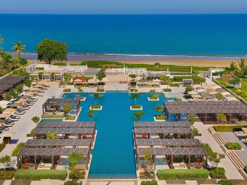 Pohled na hotelový bazén, slunečníky a moře v pozadí za slunečného dne