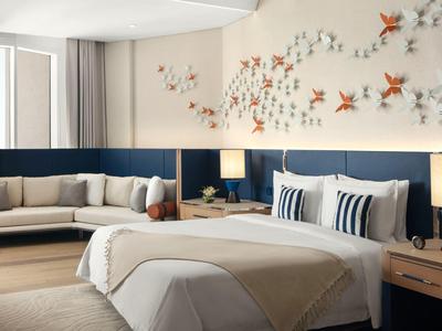 Moderní hotelový pokoj s manželskou postelí, pohovkou, dřevěnými nočními stolky a dekorativní zdí.