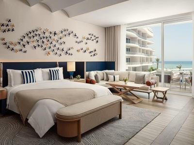 Moderní hotelový pokoj s velkou postelí, sedací částí a výhledem na moře z balkonu.