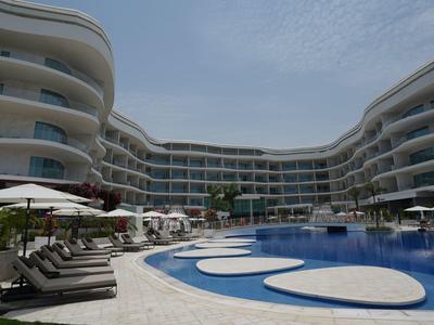 Moderní hotelový bazén s lehátky a kulatými vodními plochami pod zataženou oblohou.