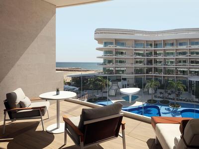 Balkon s křesly a stoly s výhledem na bazén a hotel u moře.