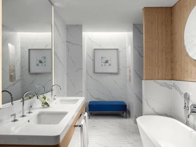 Elegantní koupelna s dvojumyvadlem, vanou a modrou lavicí u bílé mramorové stěny.