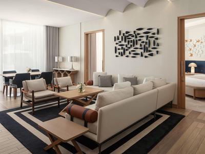 Moderní obývací pokoj se světlým nábytkem, velkými okny a výhledem do ložnice.