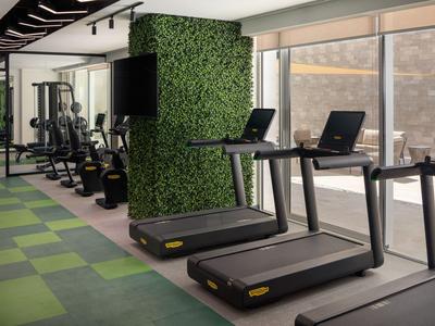 Moderne Fitnessstudio mit Laufbändern, Kardiogeräten und grünem Pflanzenwand-Design.