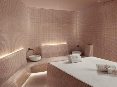 Moderní spa místnost s masážním stolkem, měkkým osvětlením a teplými béžovými dlaždicemi.